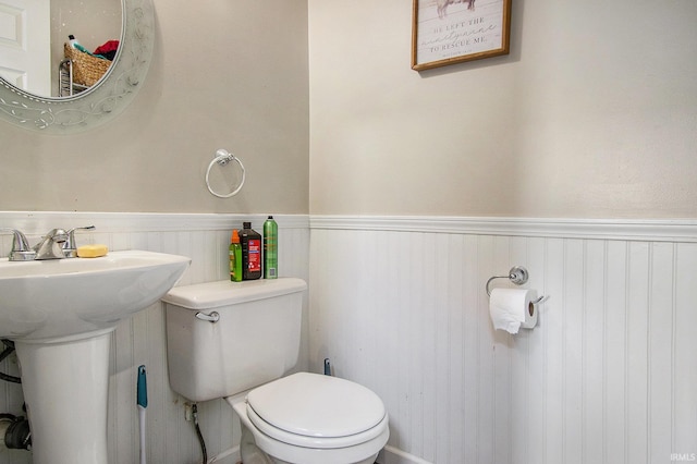 half bath featuring a wainscoted wall, toilet, and a sink