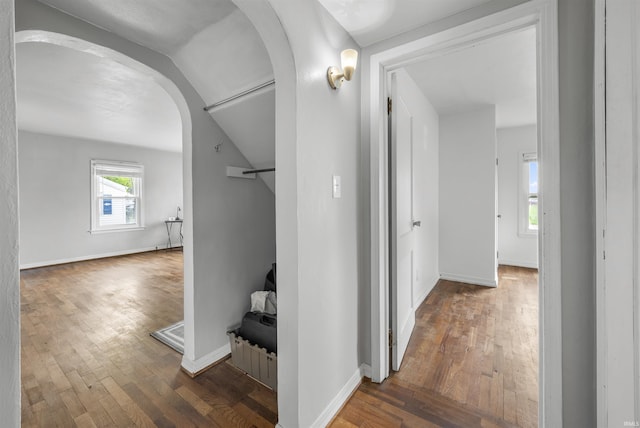 hallway with arched walkways, wood-type flooring, vaulted ceiling, and baseboards