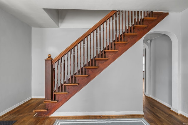 staircase featuring wood finished floors, baseboards, and arched walkways