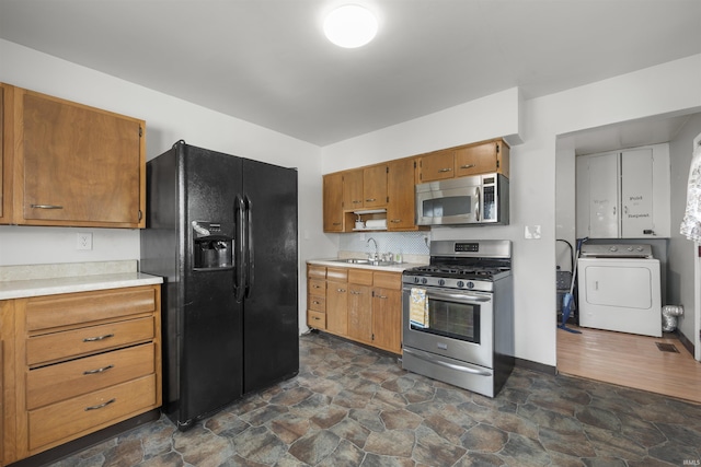 kitchen featuring washer / clothes dryer, appliances with stainless steel finishes, a sink, light countertops, and dark stone finish floors
