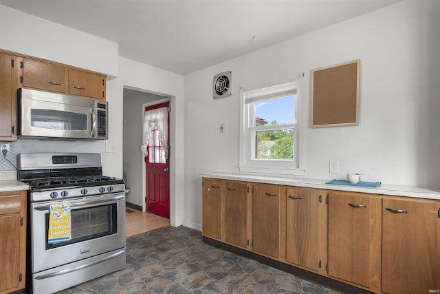 kitchen featuring appliances with stainless steel finishes, light countertops, dark stone finish floors, and brown cabinetry