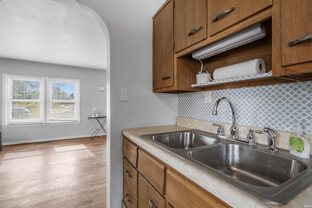 kitchen with a sink, brown cabinetry, arched walkways, baseboards, and light wood-type flooring