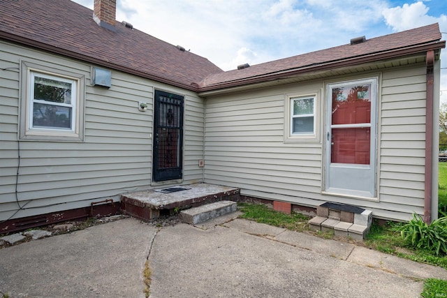 property entrance featuring a patio area, a shingled roof, and a chimney