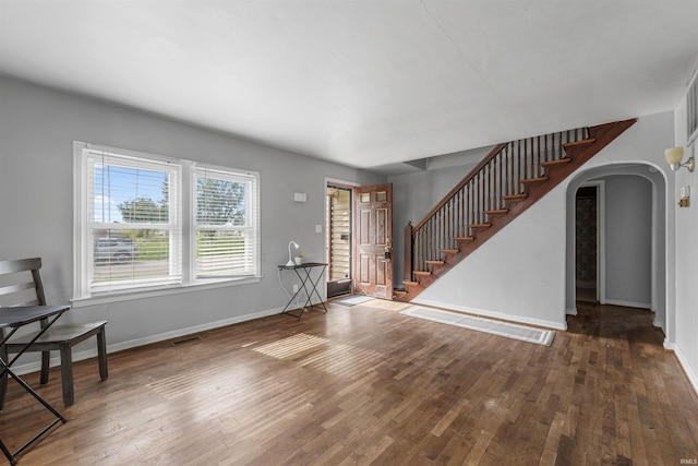 unfurnished living room featuring arched walkways, wood finished floors, baseboards, and stairway