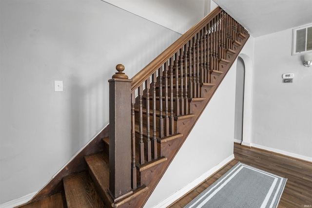 stairway with wood finished floors, arched walkways, and baseboards