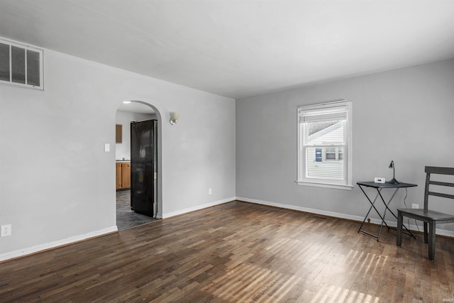 spare room with arched walkways, dark wood-style flooring, and baseboards