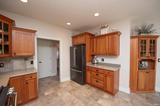 kitchen featuring high end black fridge, light countertops, glass insert cabinets, brown cabinets, and tasteful backsplash
