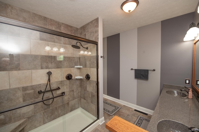 bathroom featuring a shower stall, baseboards, a textured ceiling, and double vanity