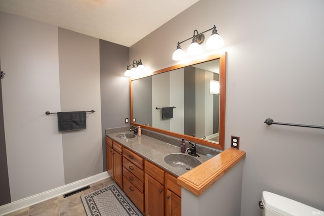 bathroom with toilet, double vanity, baseboards, and tile patterned flooring