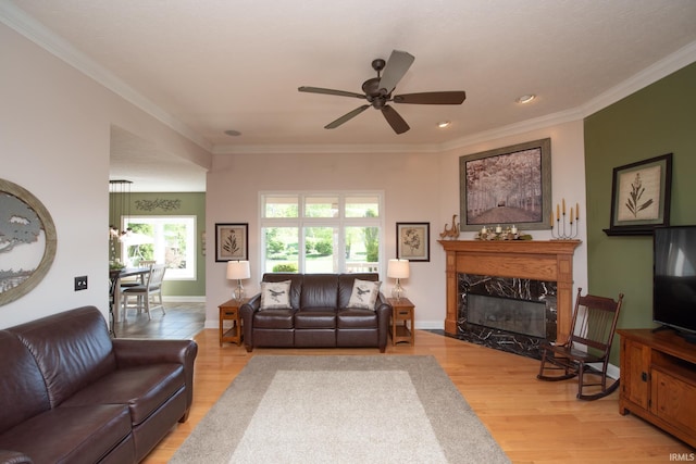 living room featuring ceiling fan, a premium fireplace, crown molding, light wood-type flooring, and recessed lighting