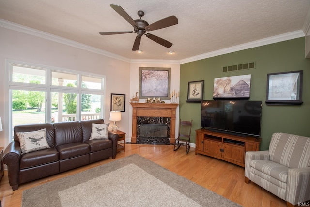 living area with crown molding, a fireplace, wood finished floors, a ceiling fan, and baseboards