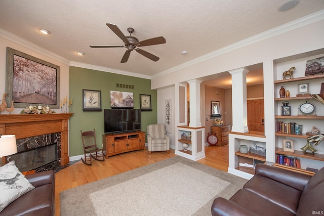 living room featuring ornate columns, wood finished floors, a ceiling fan, ornamental molding, and a high end fireplace