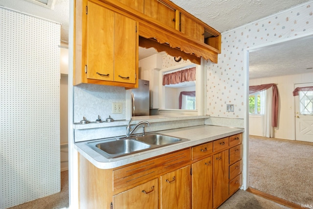 kitchen featuring a sink, a textured ceiling, freestanding refrigerator, light colored carpet, and light countertops