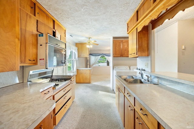 kitchen with a sink, washing machine and clothes dryer, light countertops, ceiling fan, and light colored carpet