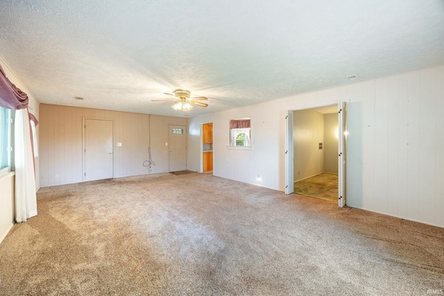 unfurnished bedroom featuring carpet floors, ceiling fan, a textured ceiling, and wood walls
