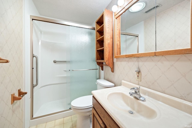 bathroom with a stall shower, toilet, vanity, wallpapered walls, and a textured ceiling