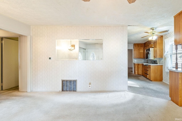 unfurnished living room with a ceiling fan, wallpapered walls, light colored carpet, a textured ceiling, and baseboards