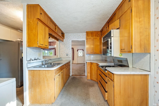 kitchen featuring a sink, stainless steel appliances, a textured ceiling, light countertops, and brown cabinets