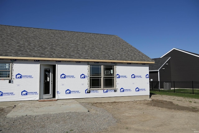 doorway to property with a shingled roof and fence