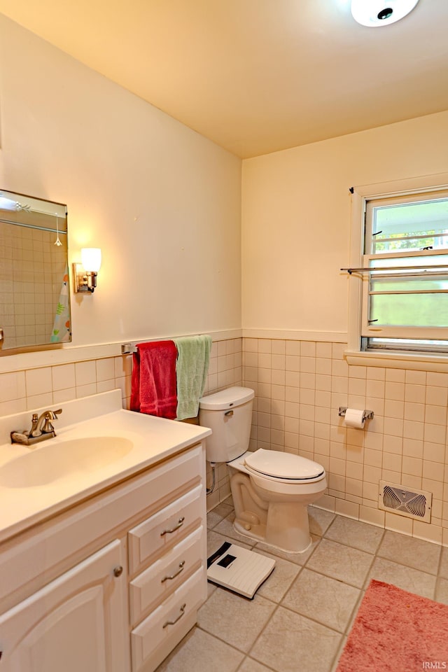 bathroom with tile walls, tile patterned floors, toilet, vanity, and wainscoting