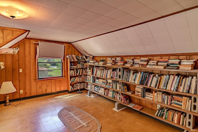 living area with wall of books, wooden walls, lofted ceiling, tile patterned floors, and baseboards