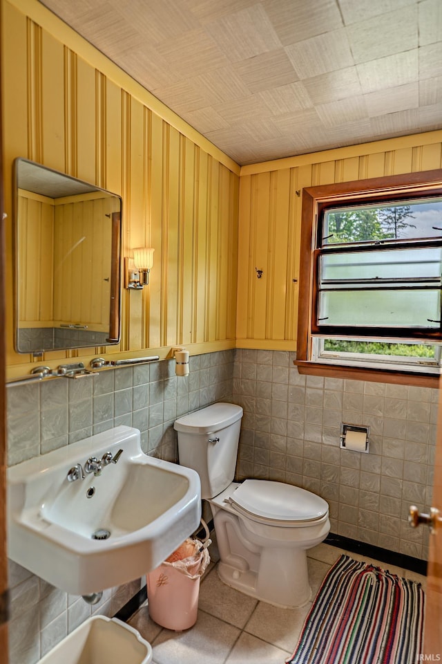 bathroom featuring toilet, tile walls, tile patterned floors, and a sink