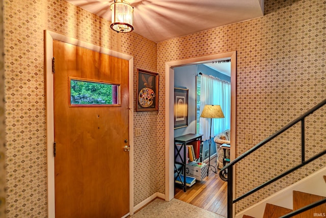 foyer entrance with wallpapered walls, wood finished floors, and baseboards
