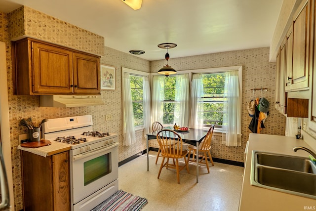 kitchen with white range with gas cooktop, a sink, extractor fan, wallpapered walls, and brown cabinets