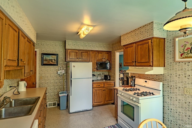 kitchen with white appliances, wallpapered walls, brown cabinetry, under cabinet range hood, and a sink