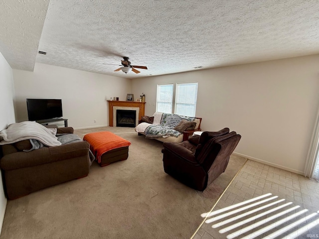 living area featuring a ceiling fan, baseboards, a fireplace with flush hearth, a textured ceiling, and carpet floors