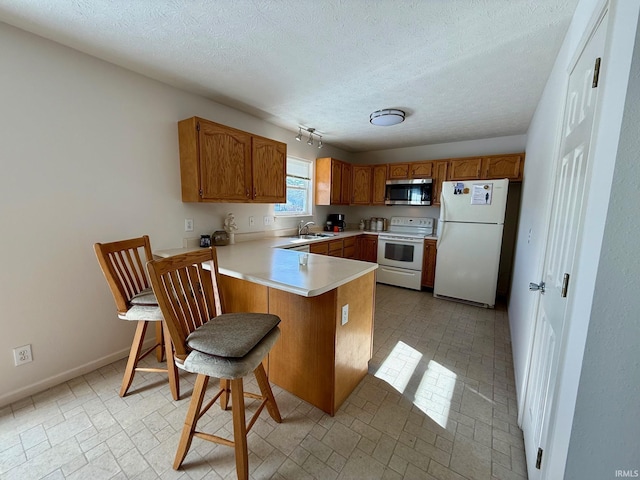 kitchen with white appliances, a sink, a peninsula, brown cabinetry, and light countertops