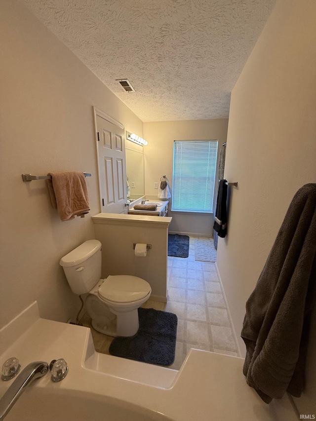 full bathroom featuring tile patterned floors, toilet, and a textured ceiling