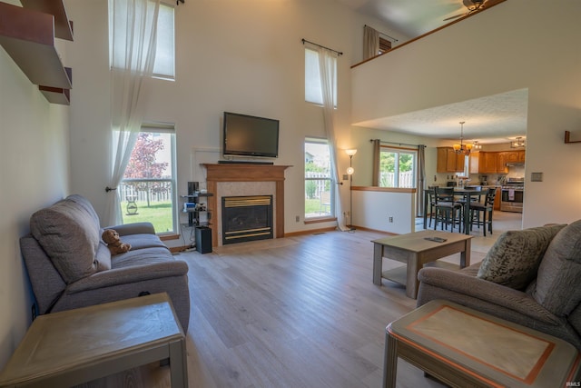living area featuring a towering ceiling, a glass covered fireplace, light wood-style floors, a chandelier, and baseboards