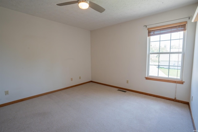 empty room with light carpet, ceiling fan, baseboards, and a textured ceiling