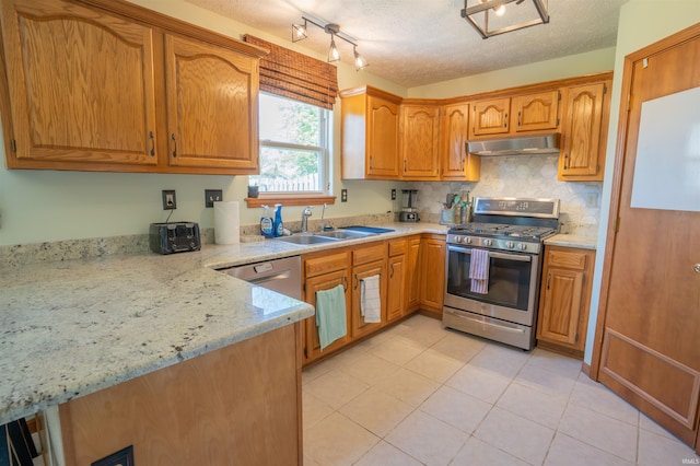kitchen featuring stainless steel range with gas cooktop, under cabinet range hood, a sink, light tile patterned flooring, and brown cabinetry