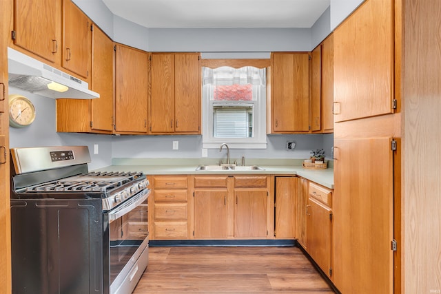 kitchen featuring stainless steel gas stove, under cabinet range hood, a sink, light wood-style floors, and light countertops