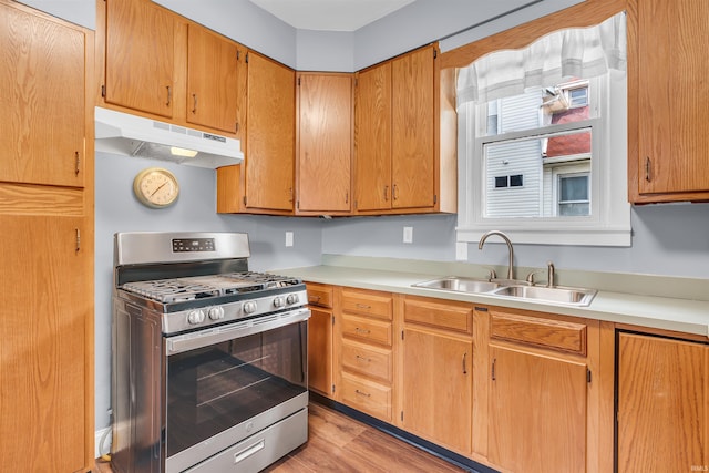 kitchen featuring gas range, under cabinet range hood, a sink, and light countertops