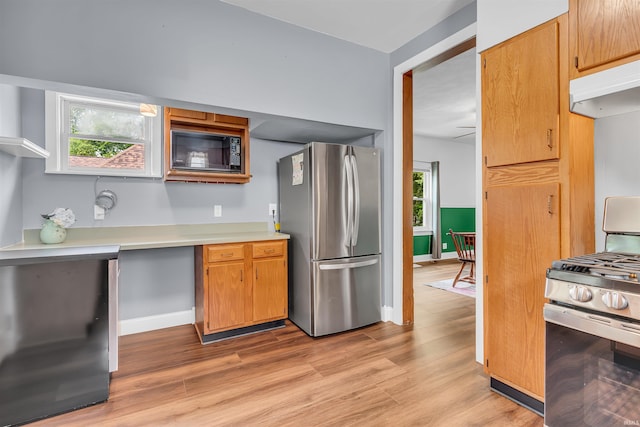 kitchen with appliances with stainless steel finishes, under cabinet range hood, light countertops, light wood-style flooring, and baseboards