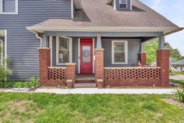 property entrance with roof with shingles, a lawn, and a porch