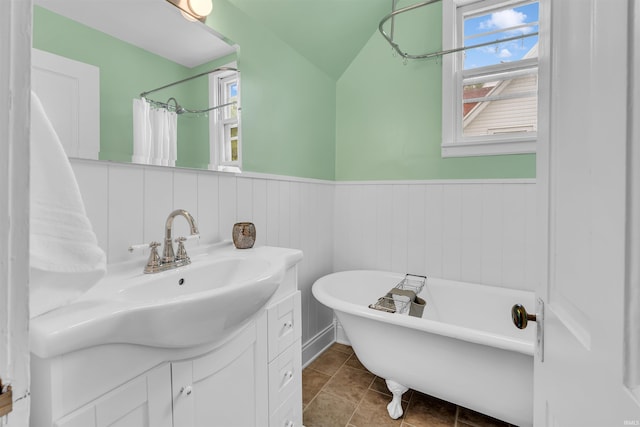 bathroom featuring vanity, a freestanding bath, wainscoting, lofted ceiling, and a shower with shower curtain
