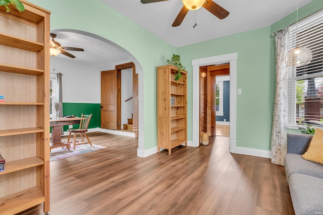 living area featuring ceiling fan, arched walkways, wood finished floors, and baseboards