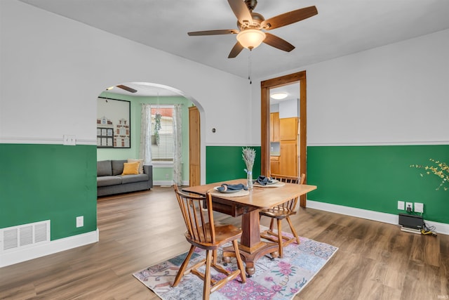 dining area featuring arched walkways, a ceiling fan, baseboards, and wood finished floors