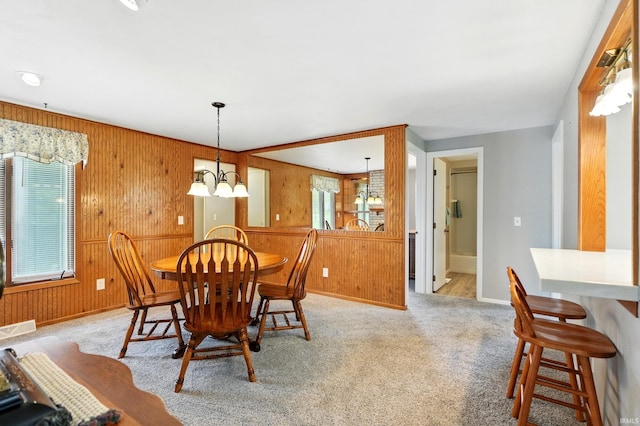 carpeted dining room with baseboards, wooden walls, and a chandelier
