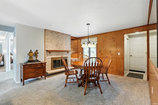 carpeted dining space with wooden walls, a chandelier, and a brick fireplace
