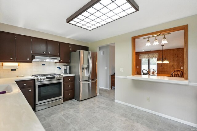 kitchen featuring stainless steel appliances, light countertops, under cabinet range hood, a chandelier, and dark brown cabinets