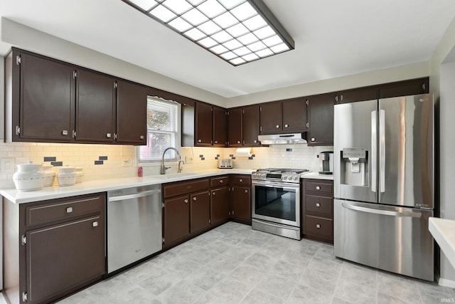 kitchen with stainless steel appliances, under cabinet range hood, a sink, light countertops, and dark brown cabinetry
