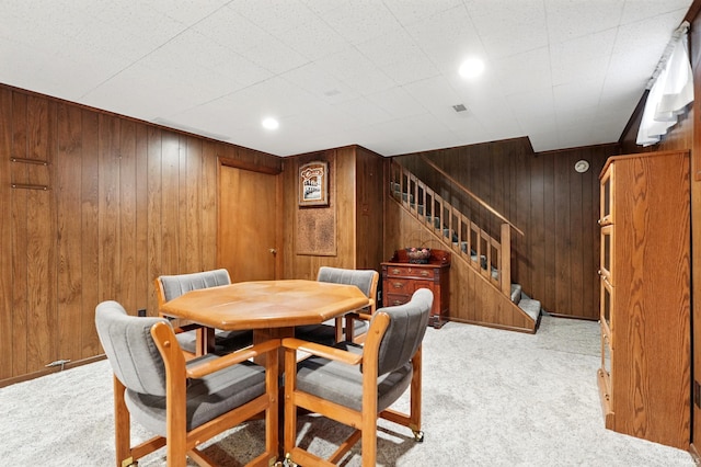 dining area featuring carpet floors, wooden walls, and stairway