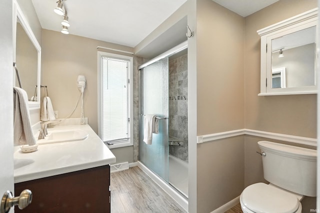 bathroom with a stall shower, toilet, wood finished floors, vanity, and baseboards