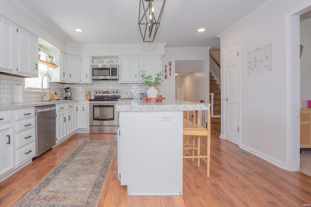 4100 Triple Crown Dr, Newburgh, IN 47630 - kitchen with appliances with stainless steel finishes, a kitchen island, tasteful backsplash, white cabinetry, and crown molding