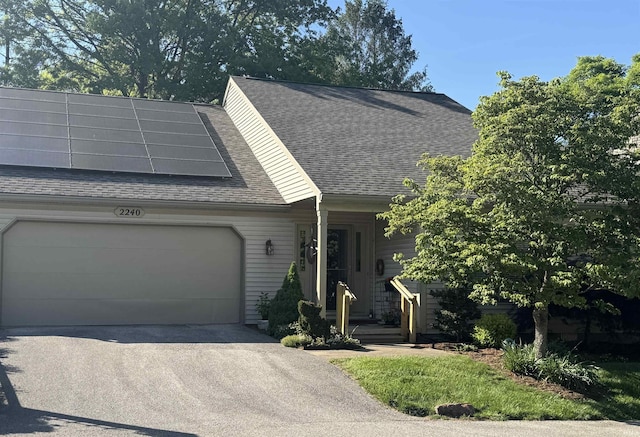 view of front of house featuring roof with shingles, solar panels, a garage, and asphalt driveway